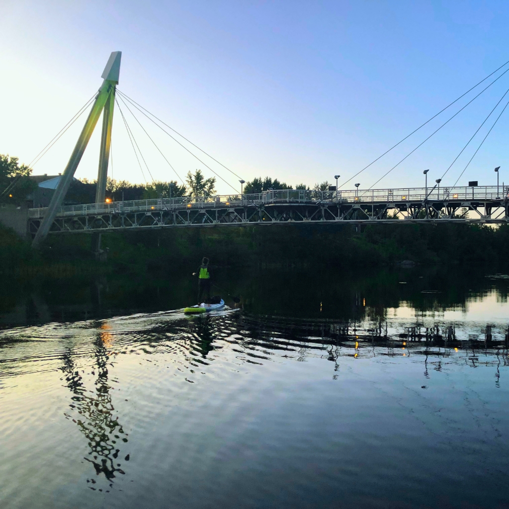 Une personne en planche à pagaie près du pont de la Rivière-aux-sables.